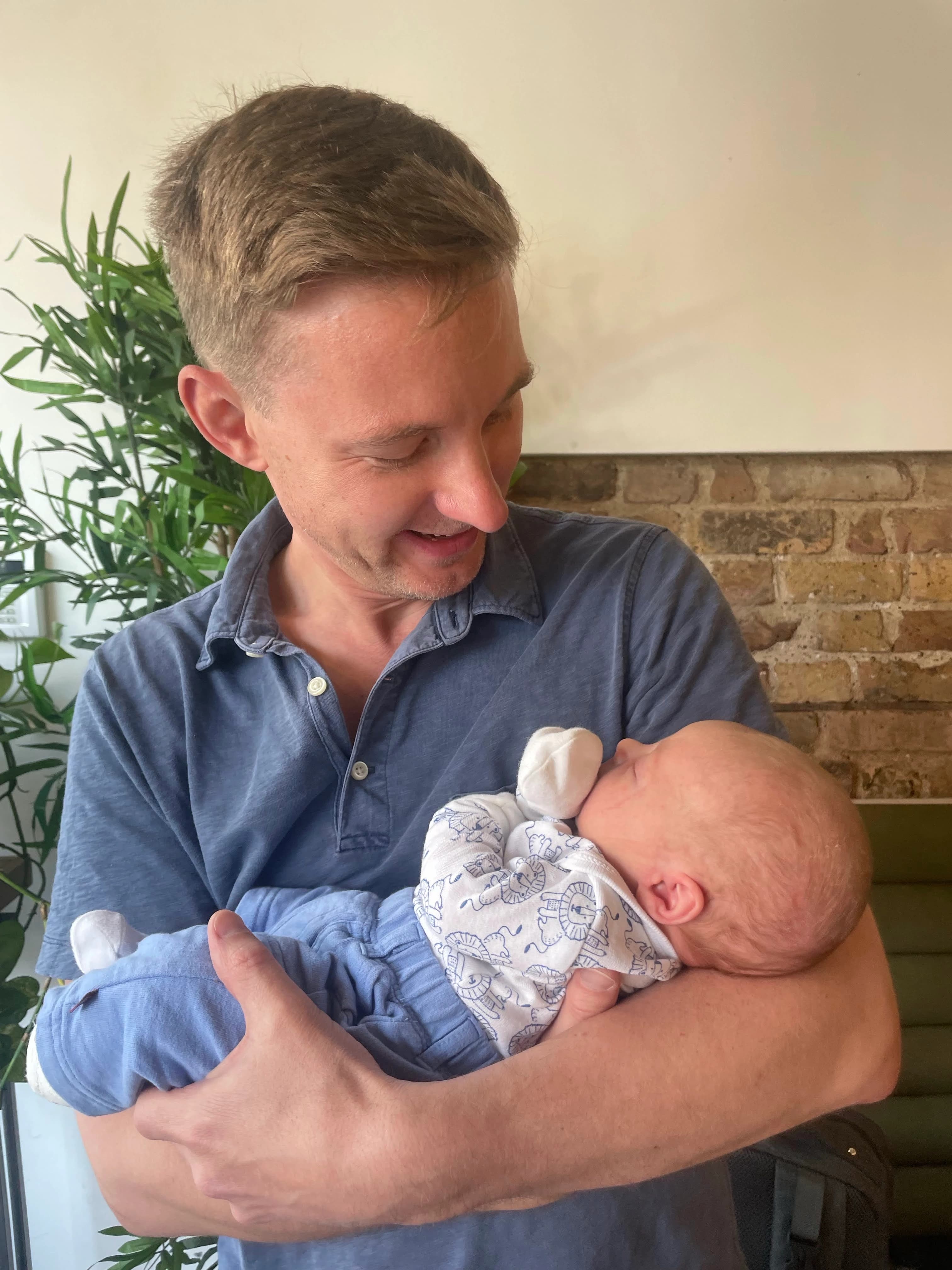 Chris holding his newborn son, asleep against his chest.